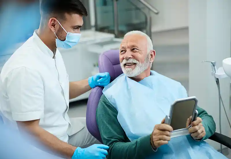 A dentist helps a man in chair with mirror